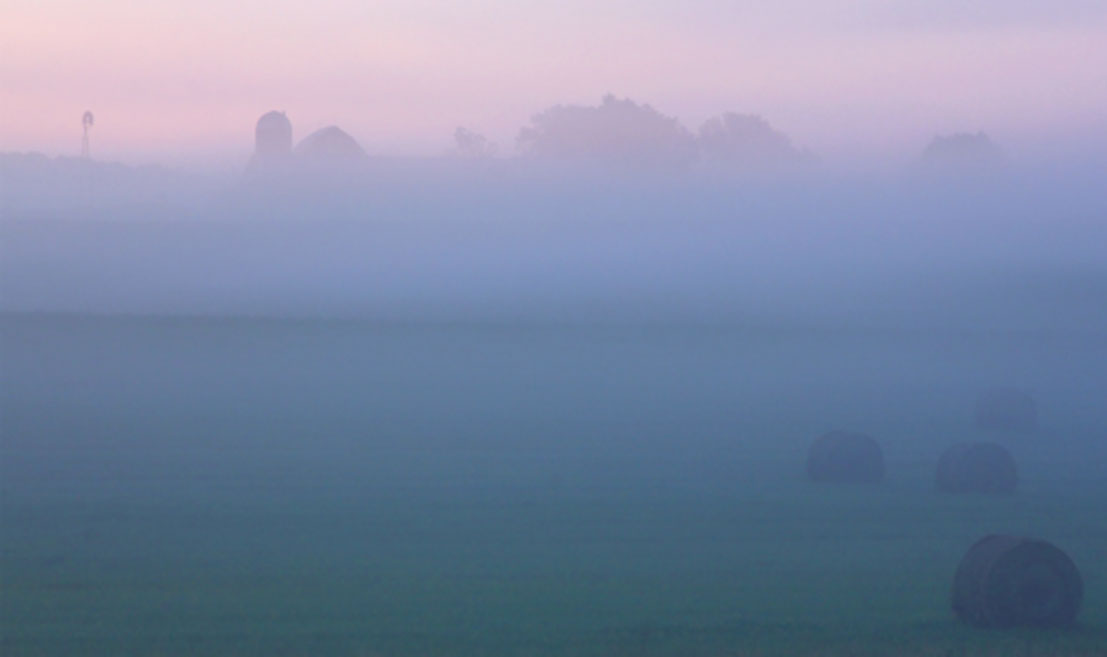 foggy sunset over farmland and rolled hay